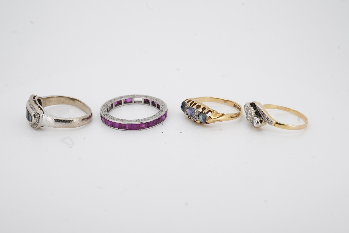 A yellow metal and illusion set three stone diamond crossover ring, size I, an 18ct, sapphire and diamond chip set ring, a modern 18ct gold and six stone sapphire set ring, with diamond chip border and an engraved white